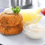 Crispy salmon croquettes with dill sauce and lemon wedges, a perfect seafood appetizer.